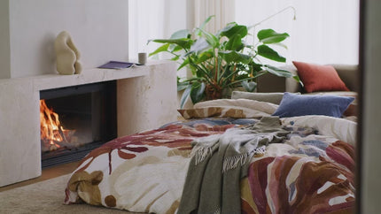 Vandyck beddengoed collectie najaar 2026 - dekbedovertrek Earthbound dessin van grote bladeren in warme tinten met blauwe accenten - bijpassende groene sprei en sierkussens in rood en blauw